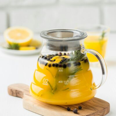 A close-up of a refreshing yellow citrus tea in a glass teapot with herbs, ideal for a healthy drink concept.