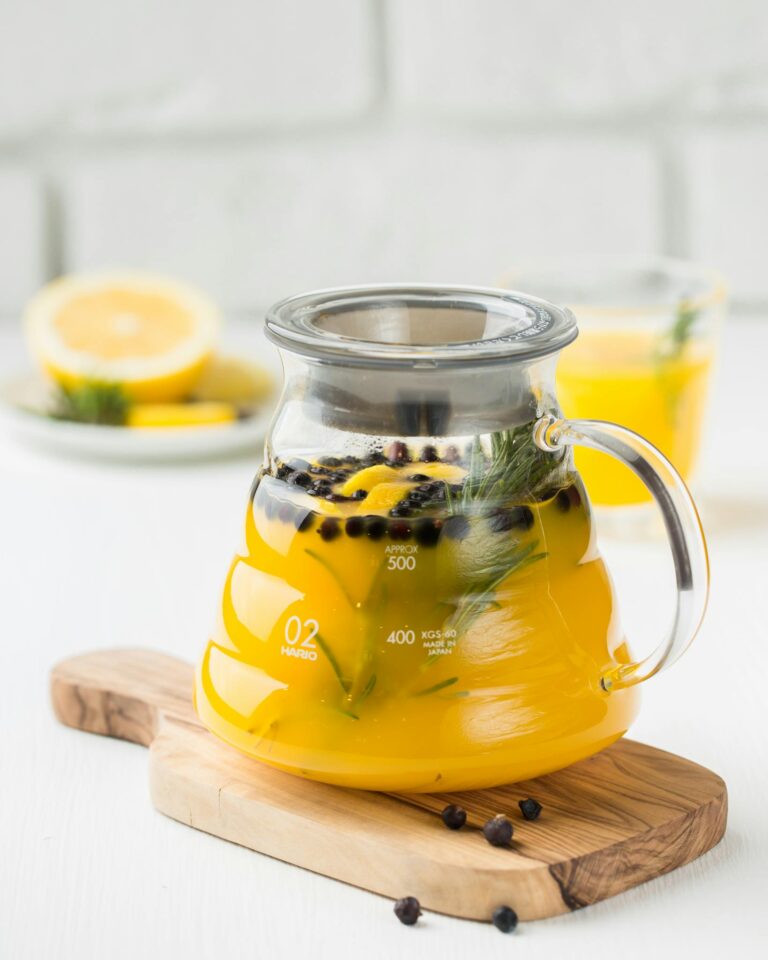 A close-up of a refreshing yellow citrus tea in a glass teapot with herbs, ideal for a healthy drink concept.