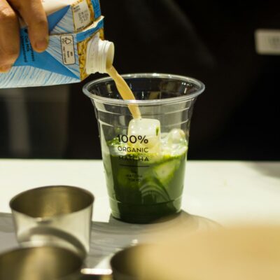 Photo by Josh Eleazar Barista pouring milk into organic matcha latte at a café counter, highlighting fresh ingredients.