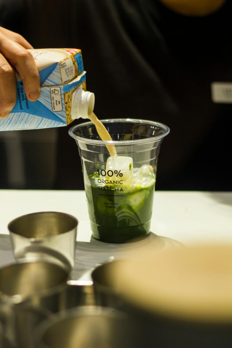 Barista pouring milk into organic matcha latte at a café counter, highlighting fresh ingredients.