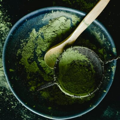 Overhead view of green matcha powder with a wooden spoon in a dark blue ceramic bowl, showcasing a rustic kitchen style.