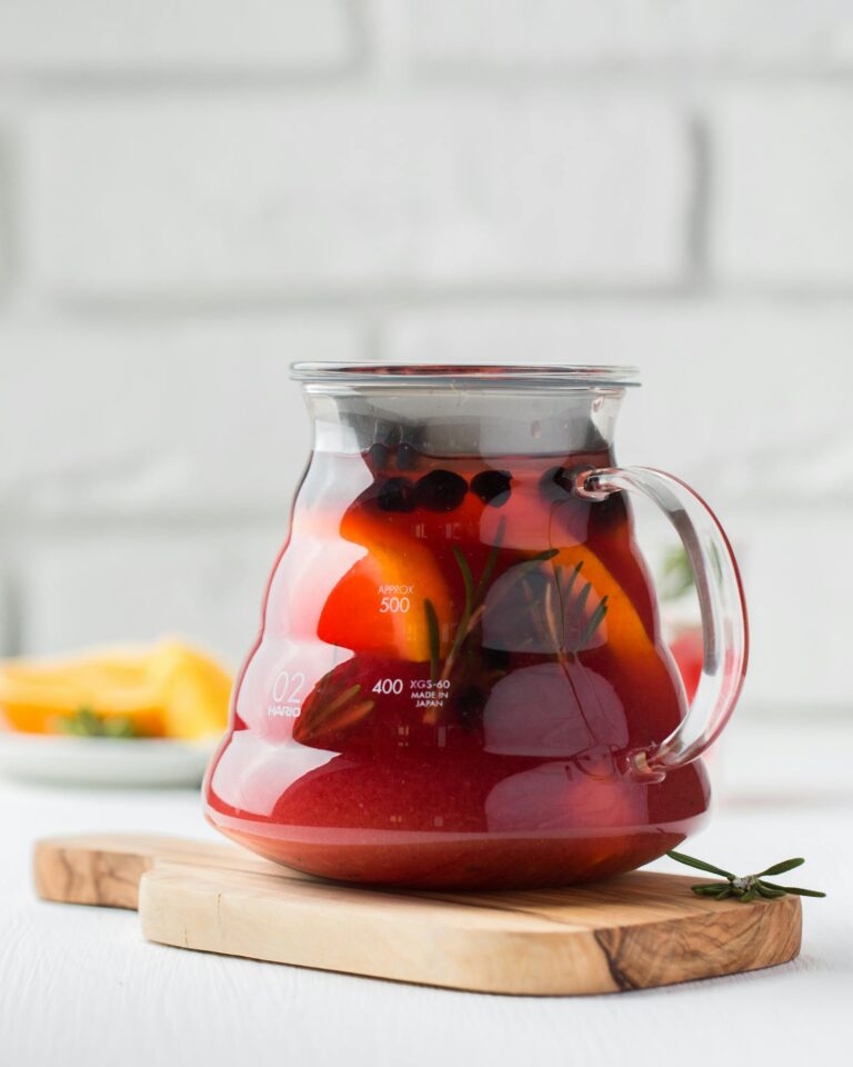 Refreshing homemade herbal tea with fruits and herbs in a glass teapot on a wooden board.