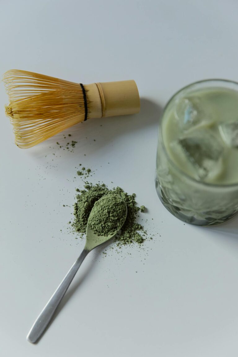 Top view of matcha latte with bamboo whisk and green tea powder.